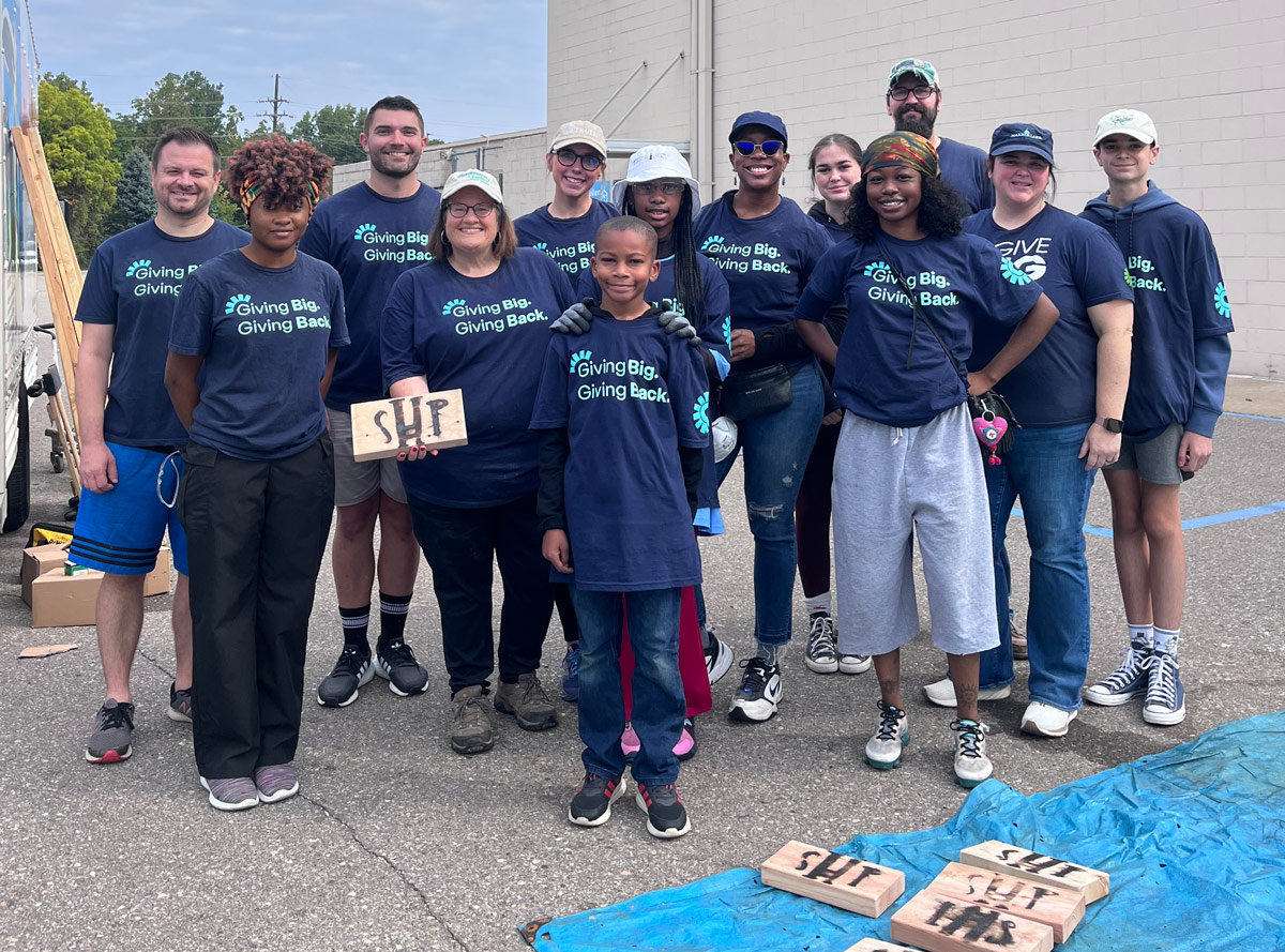 Volunteers wearing “Giving Big, Giving Back” shirts stand together after building beds for children during a community bed build event in Michigan.